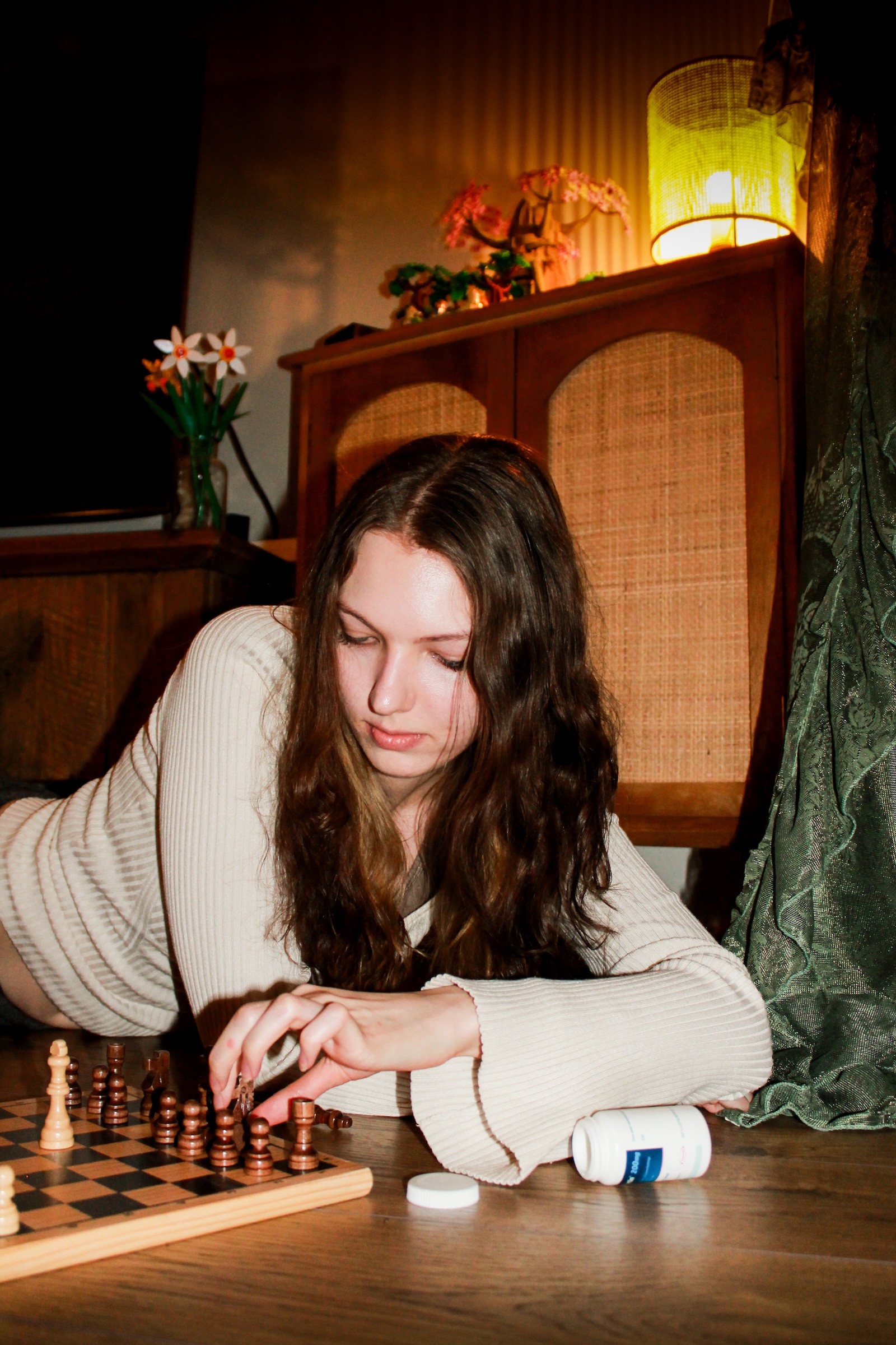 a picture of a girl playing chess in a warmly lit, vintage-style room.