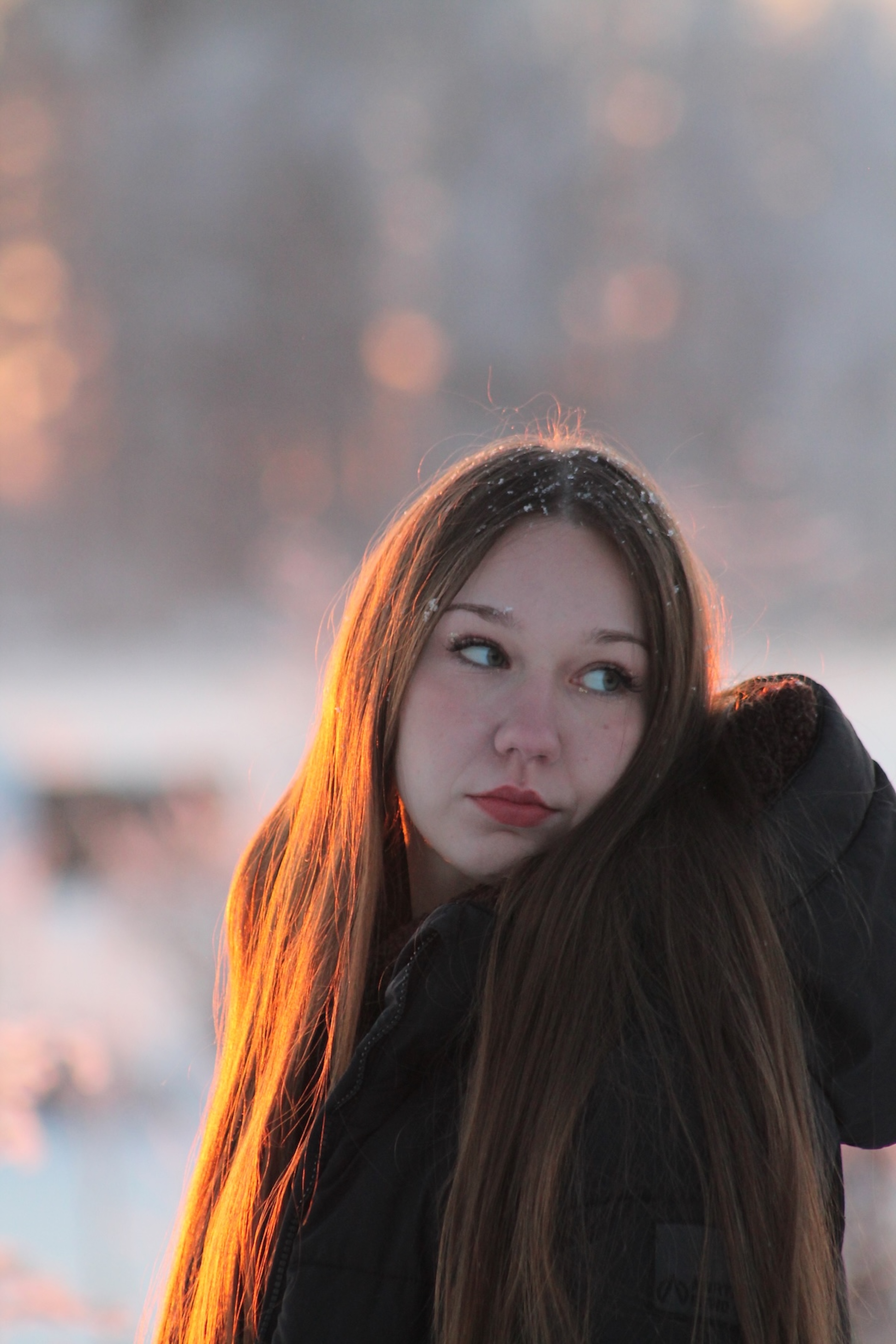 A soft-focus portrait of a young woman with long hair outdoors during sunset, with golden light illuminating her face and hair.